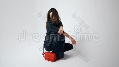 女人模特带着红色的手提包和红色的嘴唇。 美丽的模特在白色背景的照相馆摆姿势。